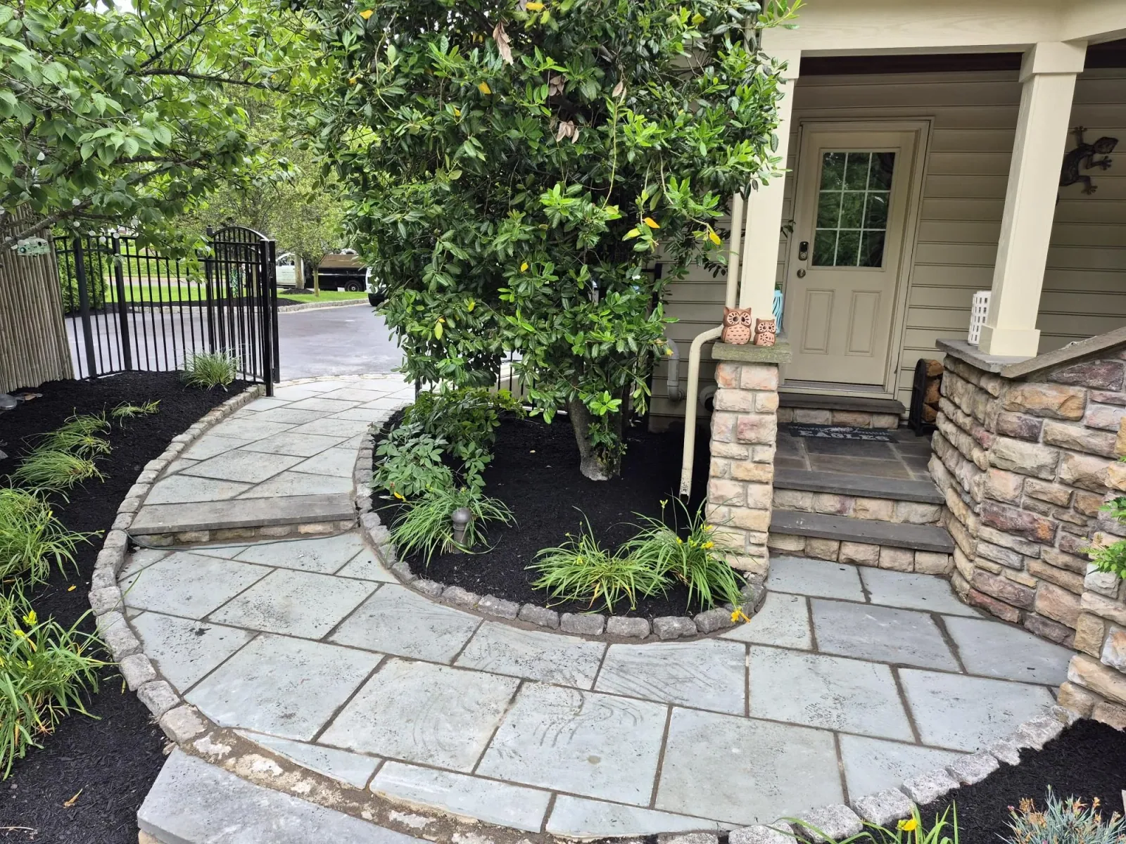 A stone walkway and planted garden beds beside a covered porch