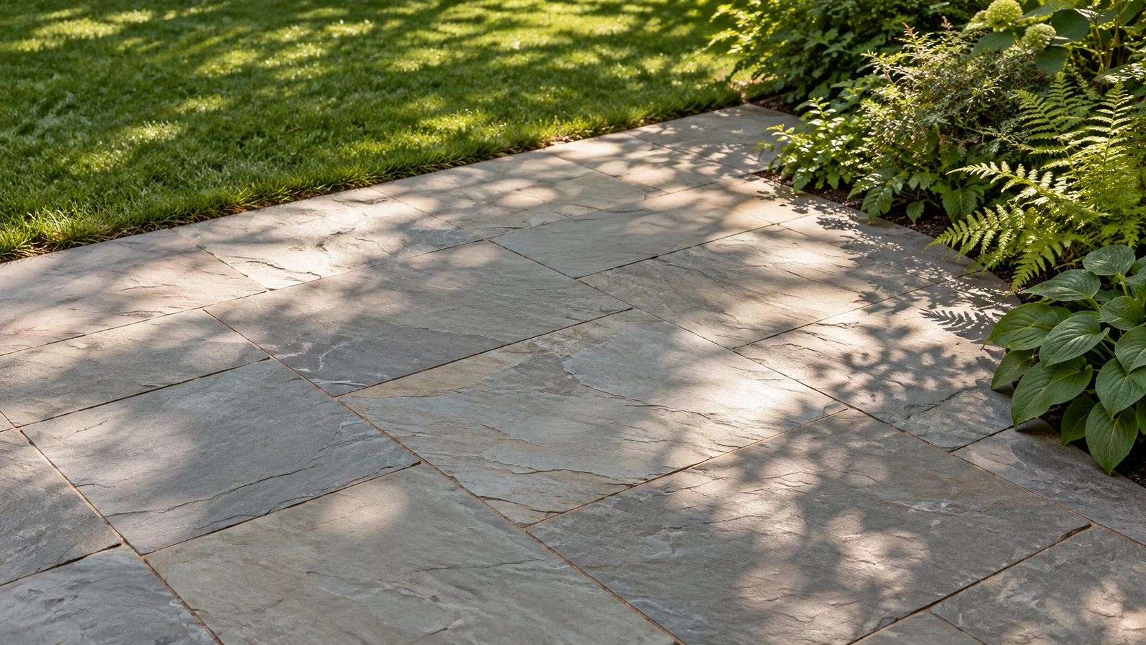 Soft tree shadows across natural bluestone beside a lush green garden