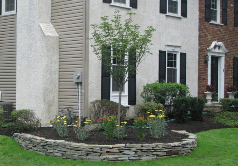 Stone wall garden with a house in background.